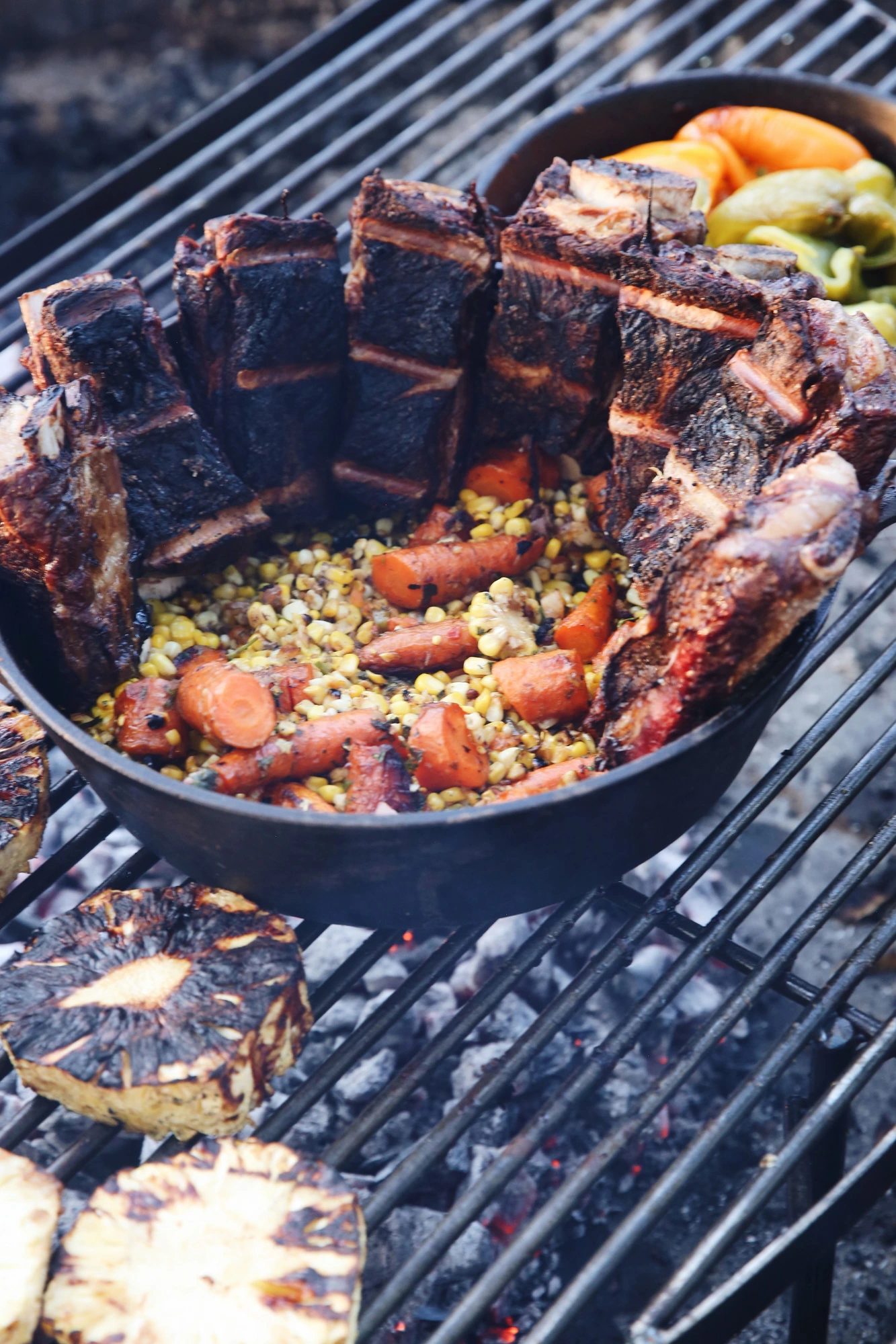 Cast iron skillet of fire-roasted short ribs, carrots, and corn relish over glowing coals
